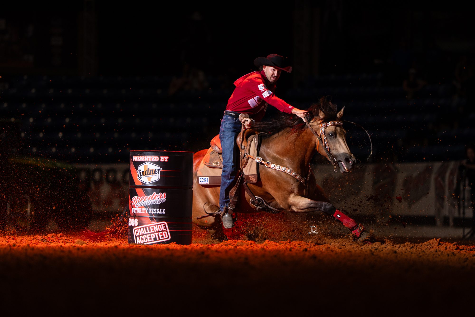 Dacota Monk barrel racing under red arena light at the Breeders Challenge, photographed by Traci Davenport